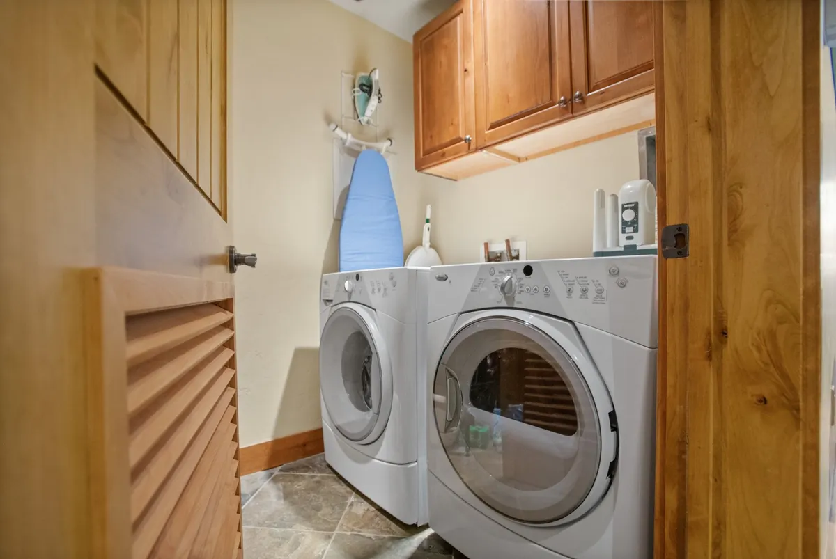 A tidy laundry area with washing machines, wooden cabinets, and an ironing board. The space is functional and organized for storing and maintaining gear and clothing after outdoor adventures.