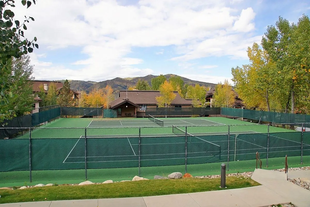 This exterior image features well-maintained tennis courts surrounded by lush green trees and nestled against a stunning mountain backdrop. The courts are clearly visible, set within a vibrant natural setting that hints at both recreational opportunities and the beauty of the surrounding Routt National Forest.