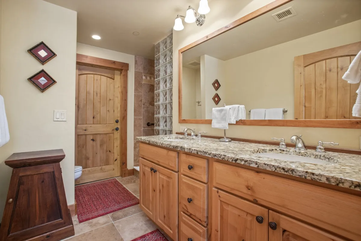 A bright bathroom with a double granite vanity, framed mirror, glass shower wall, and tasteful decor. The layout and finishes exude elegance and comfort, ideal for morning routines or unwinding in the evening.