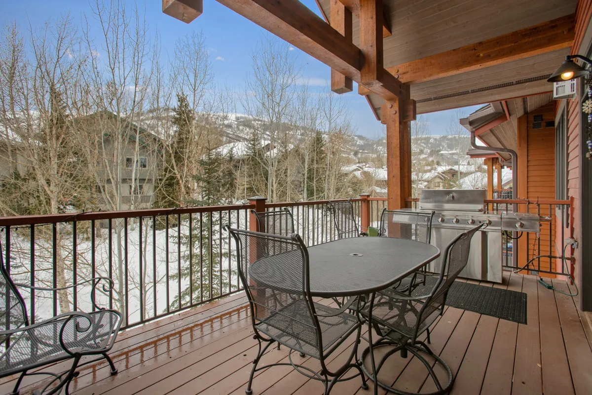 A covered outdoor deck with a dining table, grill, and panoramic mountain views framed by wooden railings. The space is perfect for al fresco dining, relaxing outdoors, or enjoying après-ski evenings with friends and family.