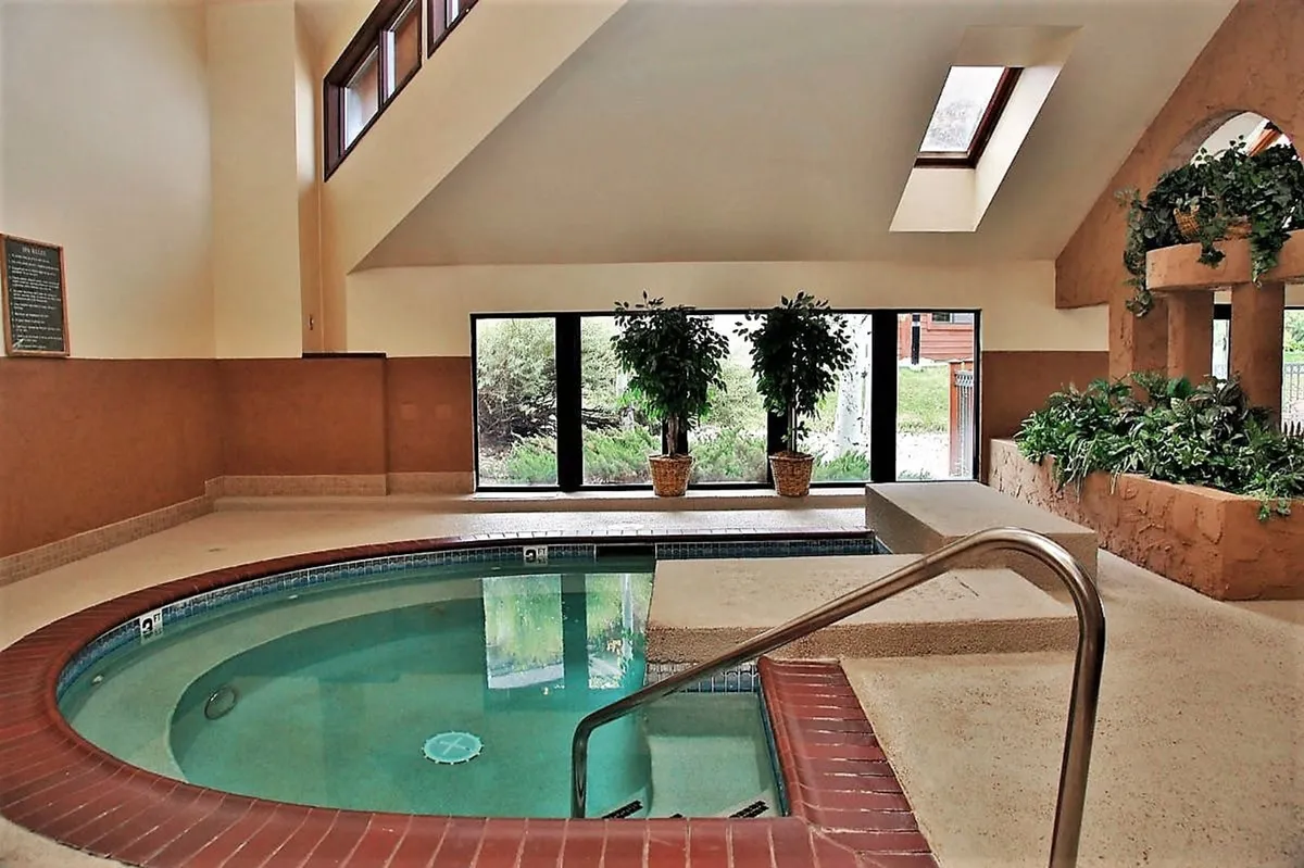 A tranquil indoor spa pool with large windows letting in natural light and lush indoor plants. The serene environment suggests wellness treatments, relaxation, and peaceful moments, capturing the essence of a day spa experience.