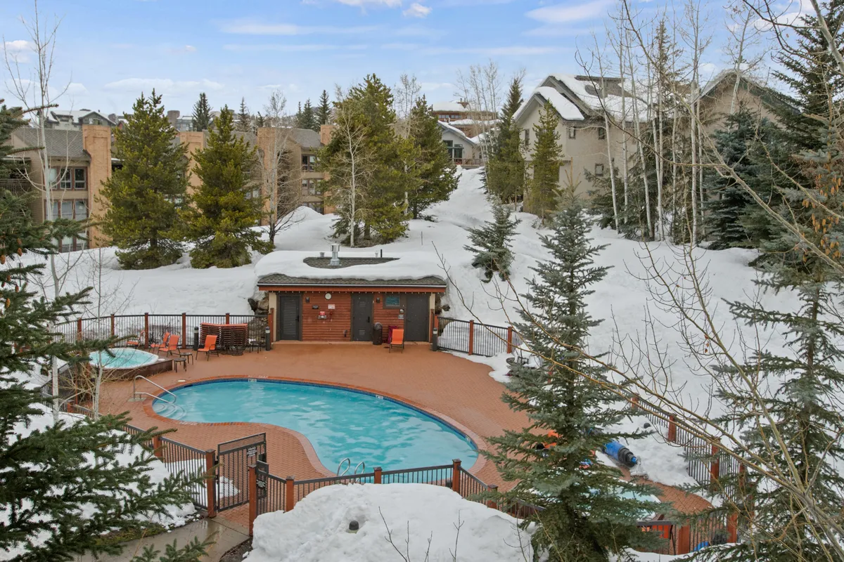An inviting outdoor swimming pool and hot tub are pictured, surrounded by snow-dusted trees and comfortable poolside lounge chairs. The scene captures both a tranquil winter atmosphere and the promise of year-round relaxation and recreation, including evenings spent soaking in the hot tub under the stars.
