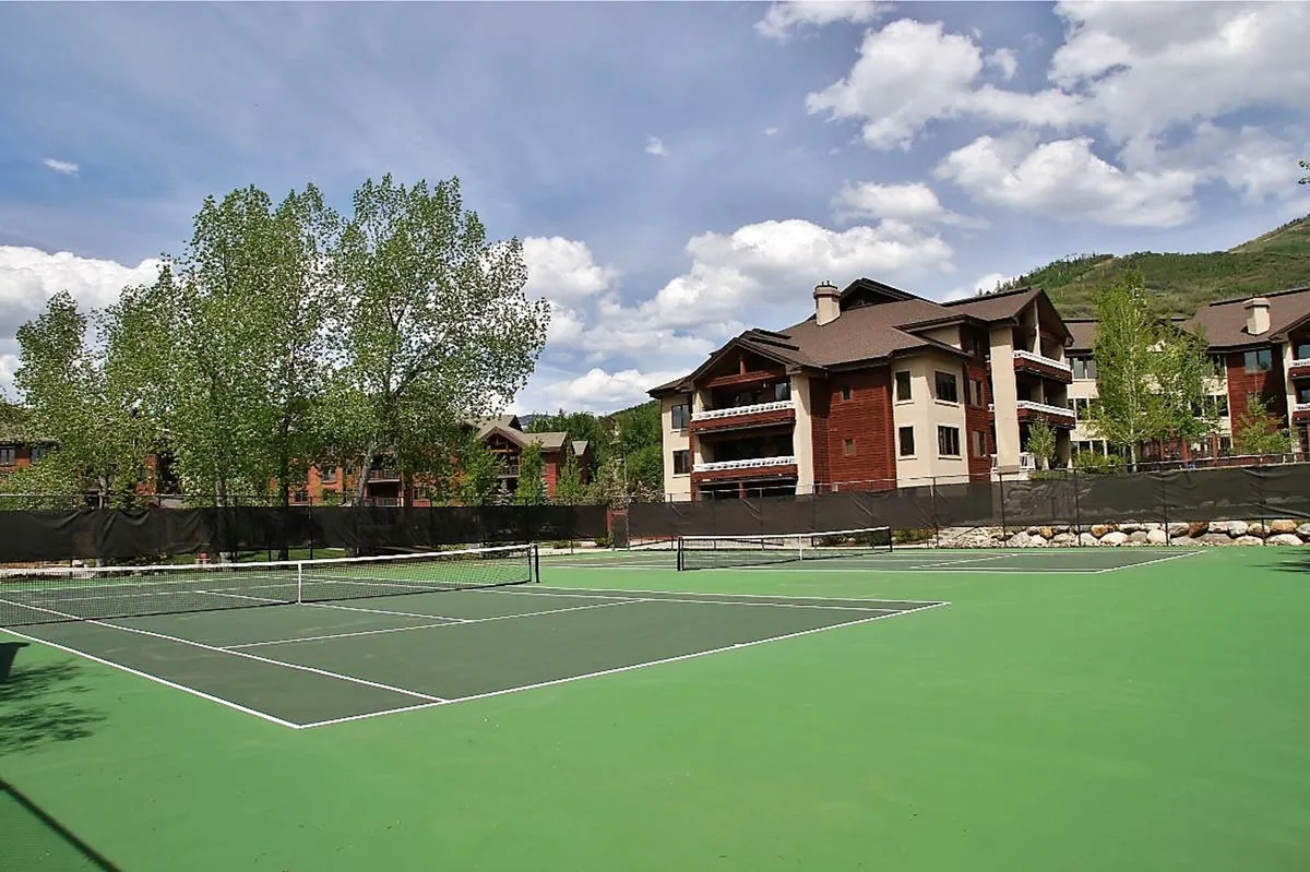 Spacious outdoor tennis courts surrounded by mature trees, with building facades in the background. The courts are ready for lively matches or casual games, inviting guests to enjoy the fresh air and social activities.