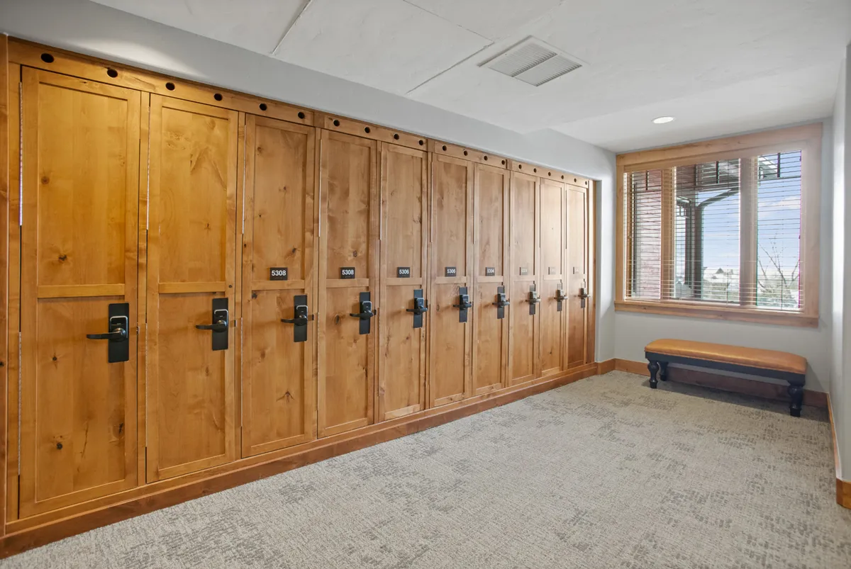 A well-organized mudroom featuring wooden lockers, a wooden bench, and a window letting in natural light. The setup is designed for storing personal items and ski gear, providing a space to get ready before or after hitting the slopes.