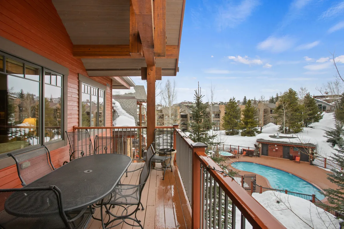 An elevated balcony view overlooking the pool area with surrounding trees and snow-covered ground. This angle offers a sense of connection between private condo spaces and the communal outdoor amenities.