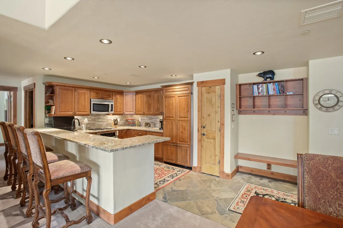 A chef’s kitchen with granite countertops, stainless steel appliances, wood cabinetry, and bar stools for casual dining. The space is bright, functional, and designed for both cooking and entertaining.